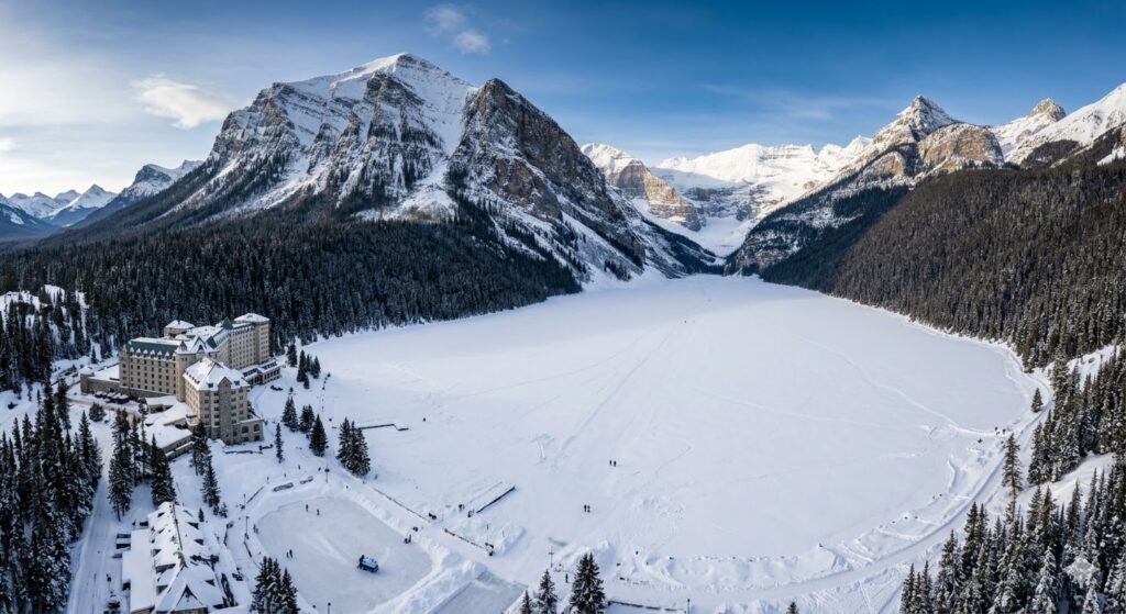 🏔️ Estações do Ano na América do Norte 2026: O Guia Completo O Lago Louise no Parque Nacional de Banff, Canadá, totalmente congelado e coberto de neve, cercado por montanhas rochosas sob um céu azul de inverno.