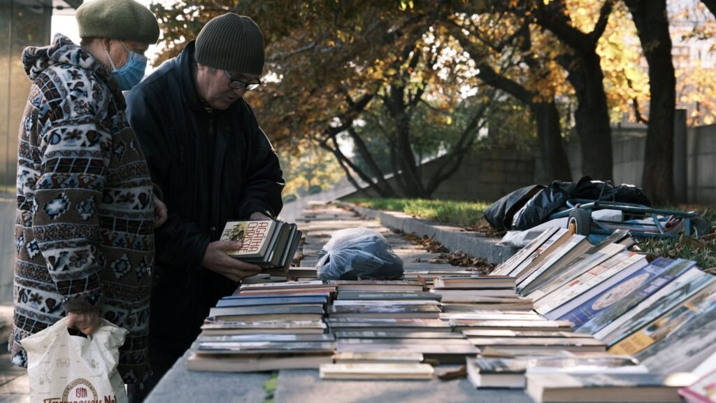 Bancada de feira ao ar livre com produtos artesanais e livros dispostos para venda em dinheiro vivo.