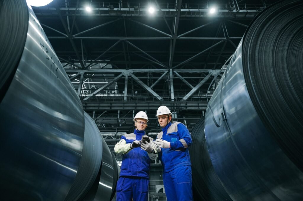 Engenheiros com capacete e uniforme azul analisando plantas e equipamentos em um galpão industrial na Rússia.