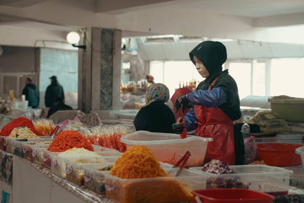Trabalhar no Uzbequistão em 2026: Visto, Salários e Vagas Trabalhadora a organizar mercadorias e especiarias num mercado coberto no Uzbequistão.